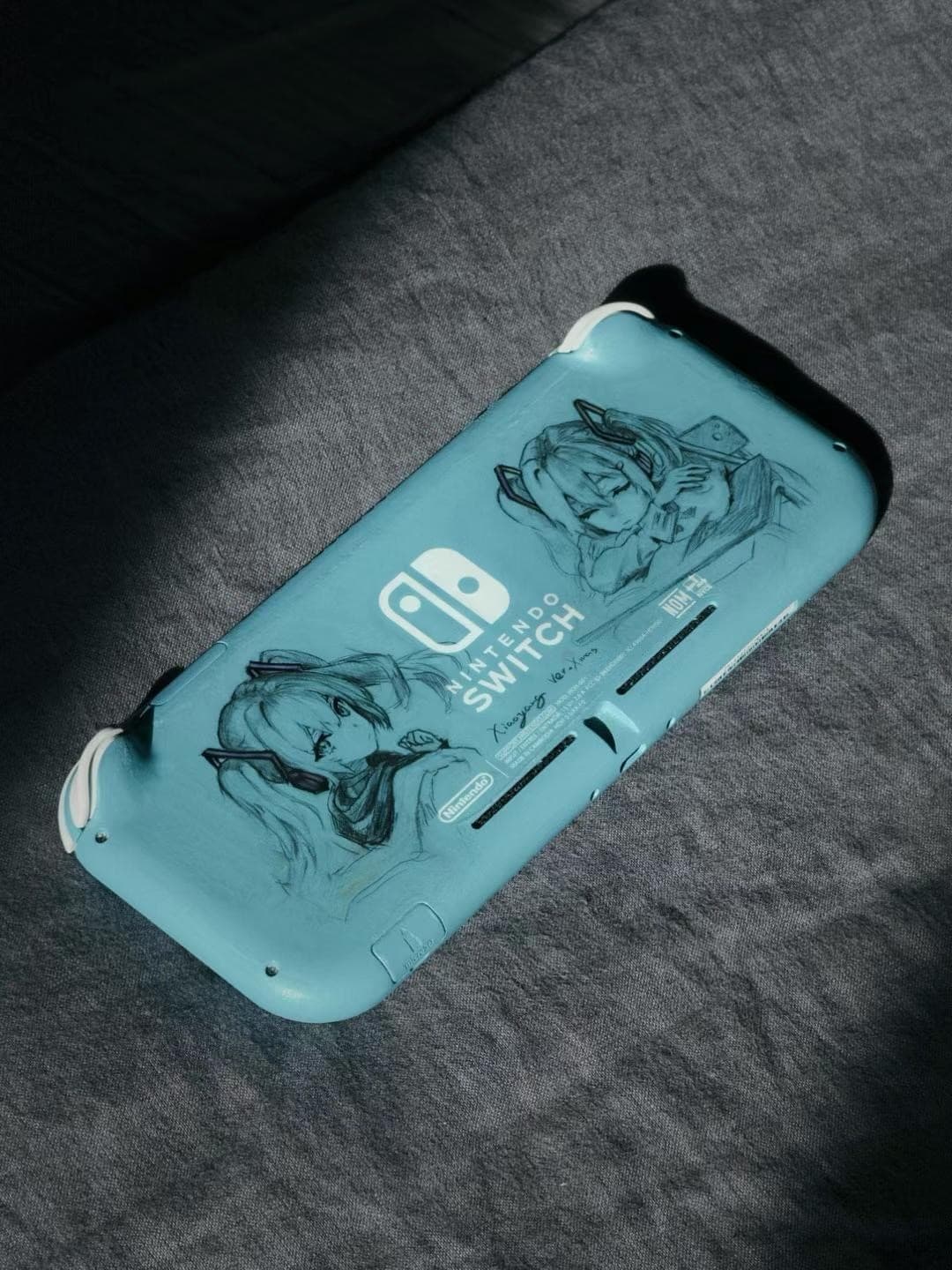 A turquoise Nintendo Switch Lite with hand-drawn Hatsune Miku on the back