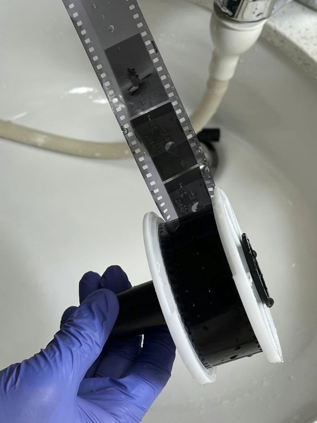 A gloved hand holding a reel of developed film above a sink